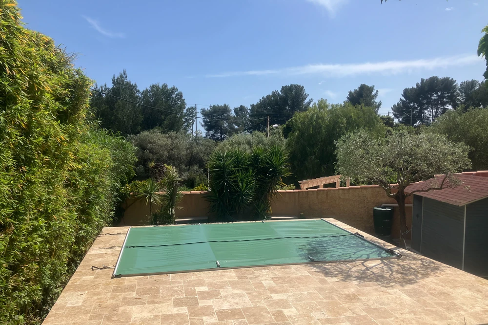 Piscine résidentielle extérieure avec bâche de sécurité verte déployée, entourée de dallage en pierre naturelle