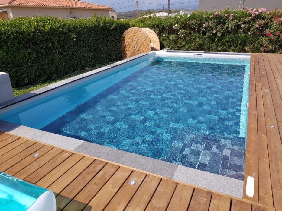 Piscine rectangulaire extérieure avec margelles en pierre claire, entourée de pelouse artificielle
