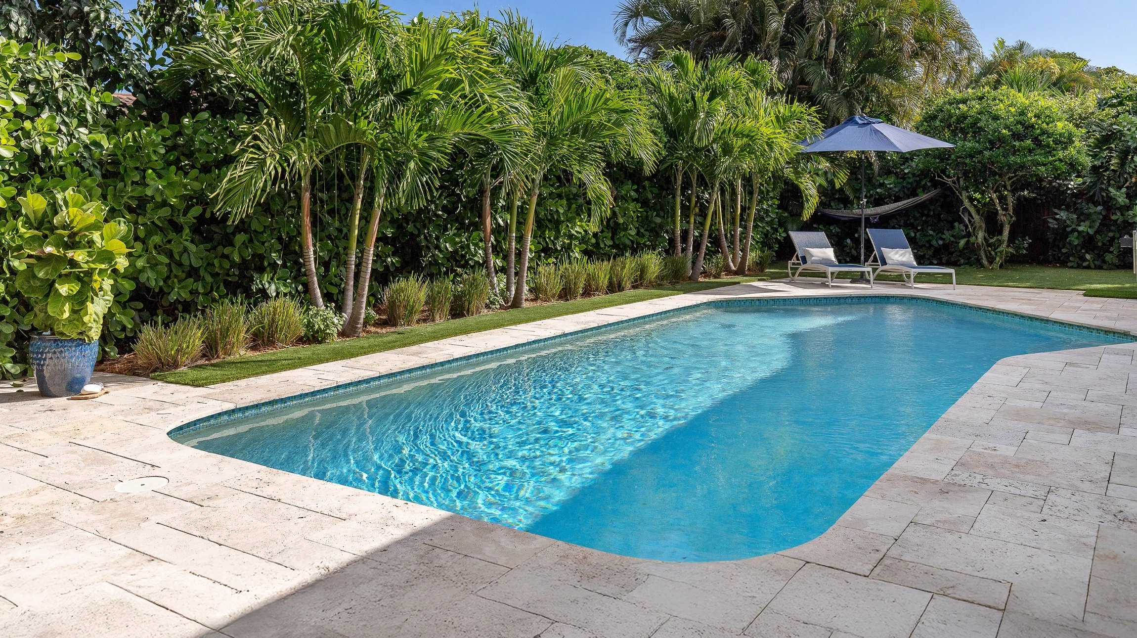 Piscine &agrave; d&eacute;bordement avec transats bleus et parasols beiges sur terrasse en bois